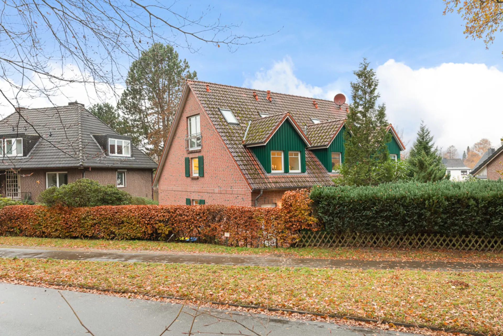 Zweistöckiges Wohnhaus mit Ziegeldach, grünen Fensterläden und umliegenden Hecken.