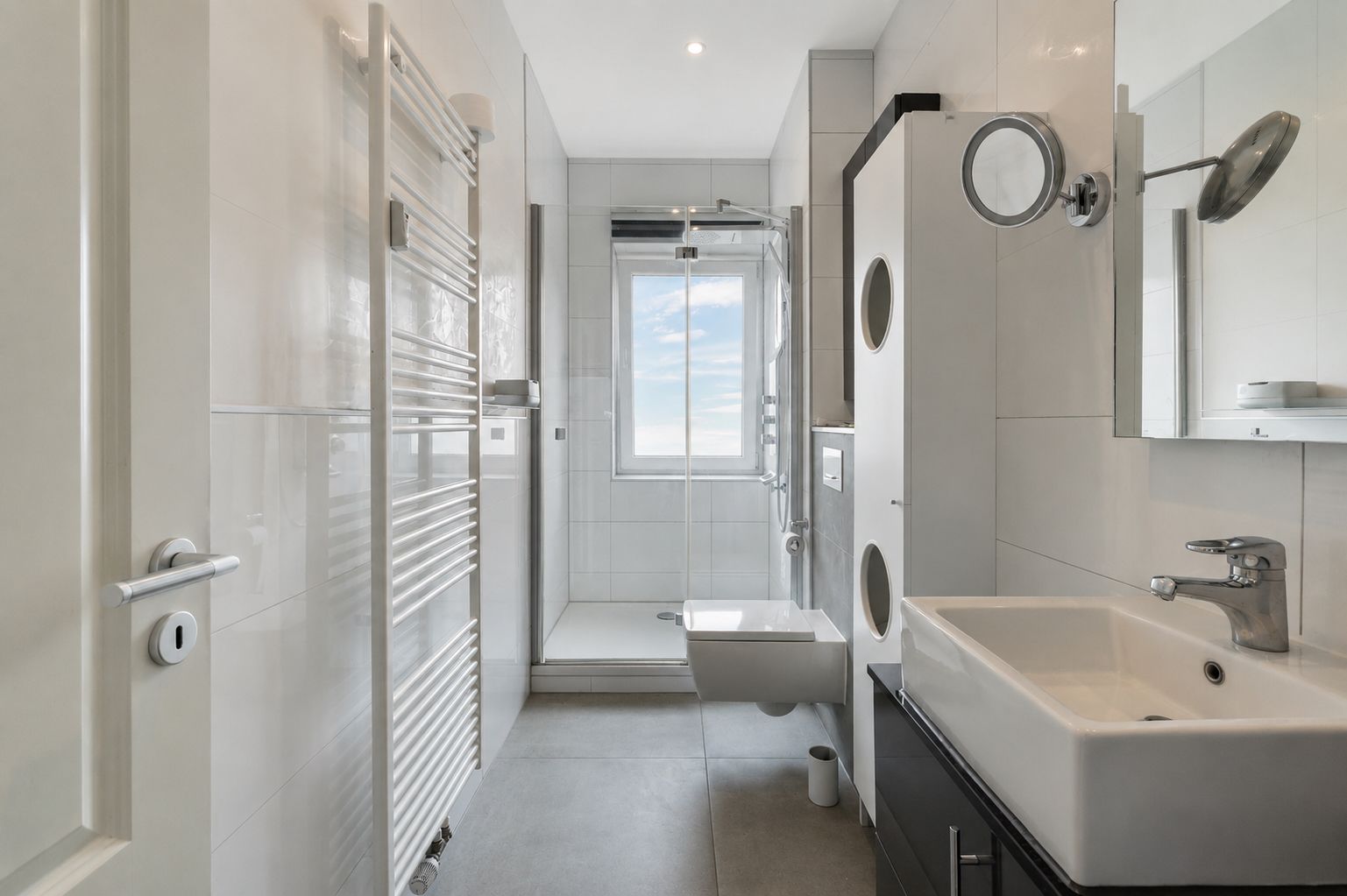 Modernes Badezimmer mit Dusche, Waschbecken, Wandspiegel und Fenster.