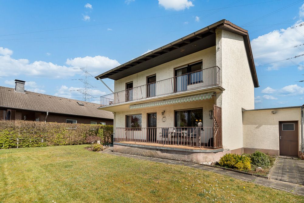 Zweistöckiges Haus mit Balkon und Terrasse, davor ein gepflegter Garten.