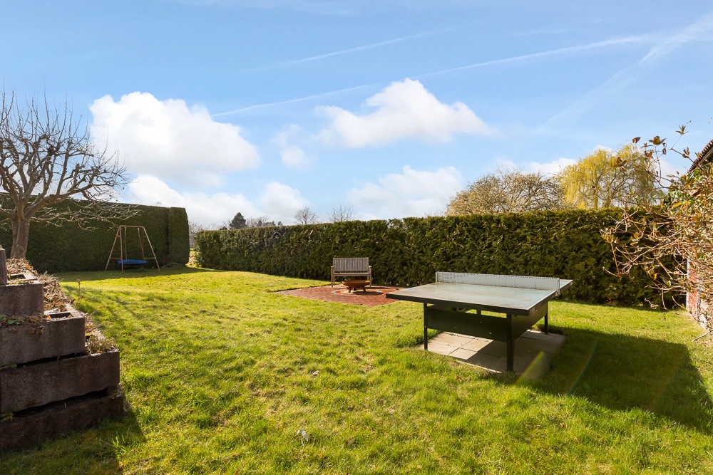 Großer Garten mit Tischtennisplatte, Sitzbank, Schaukel und Hecke im Hintergrund.