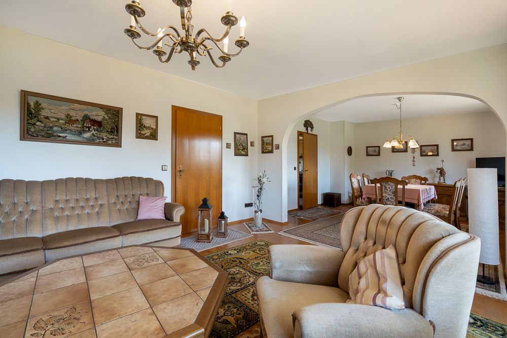 Wohnzimmer mit braunen Polstermöbeln, Holztisch, Kronleuchter und Blick ins Esszimmer.