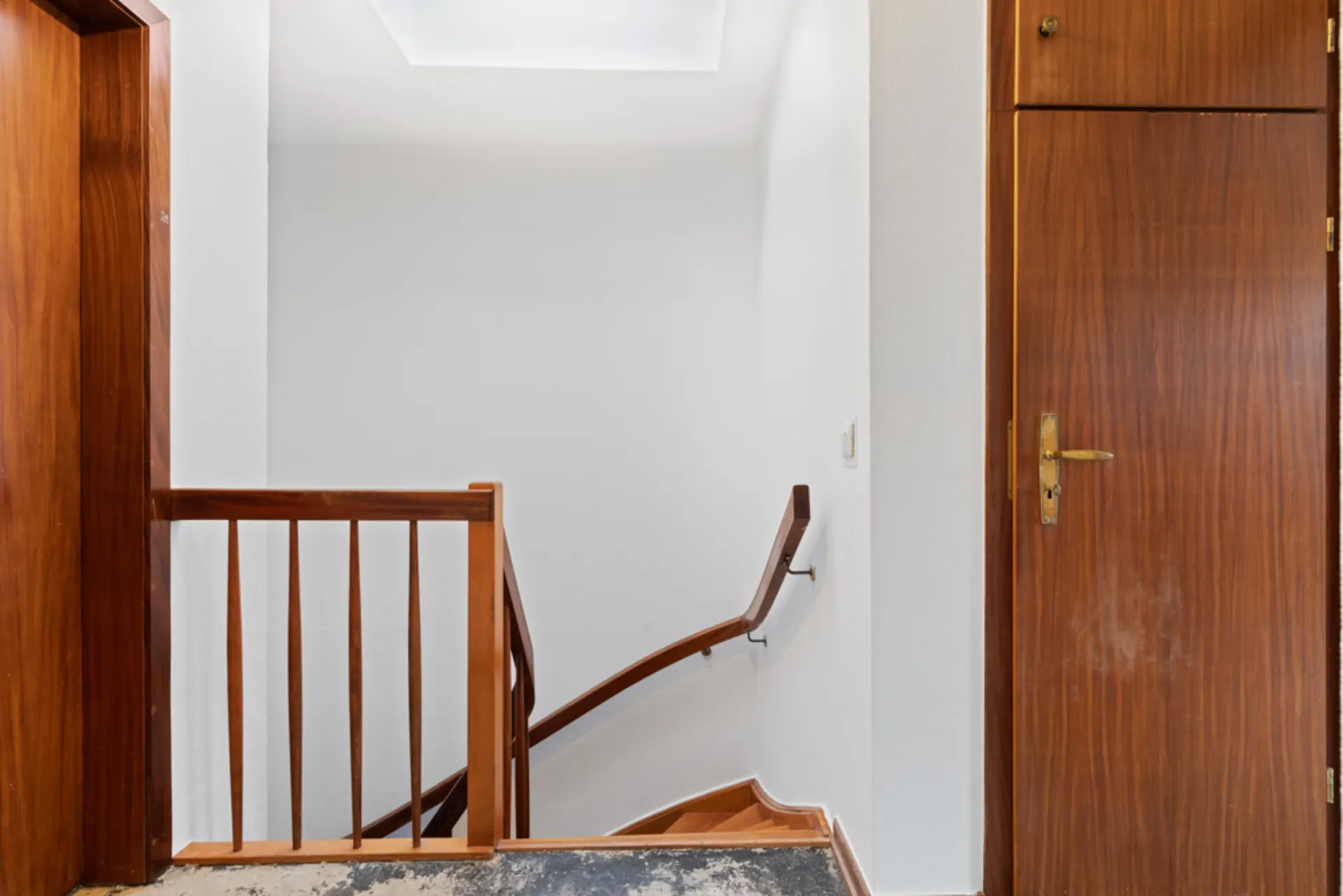 Innenraum mit Holztreppengeländer, weißer Wand und Holztür auf der rechten Seite.
