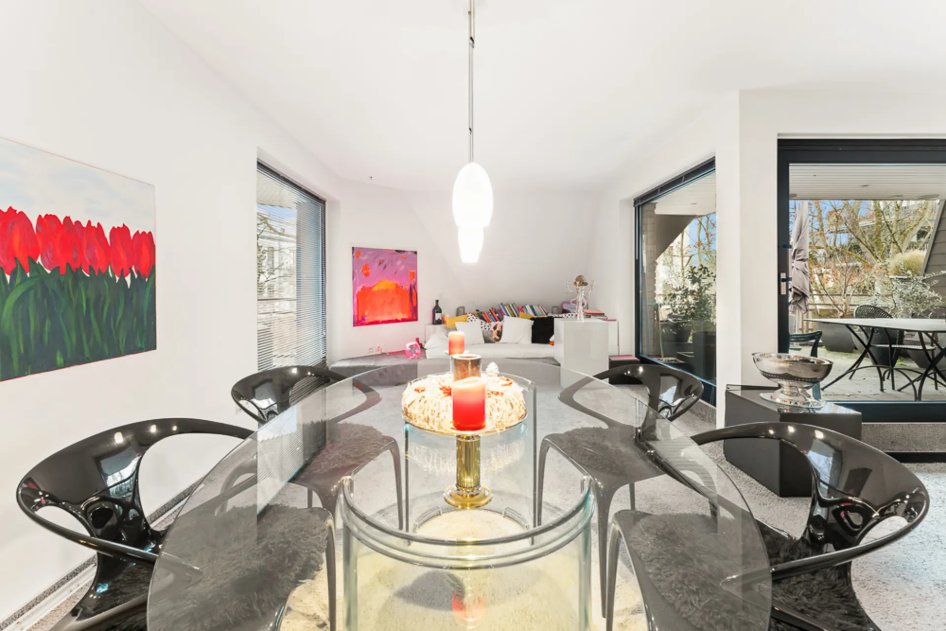 Heller Essbereich mit Glastisch, schwarzen Stühlen, Bildern und Zugang zur Terrasse.