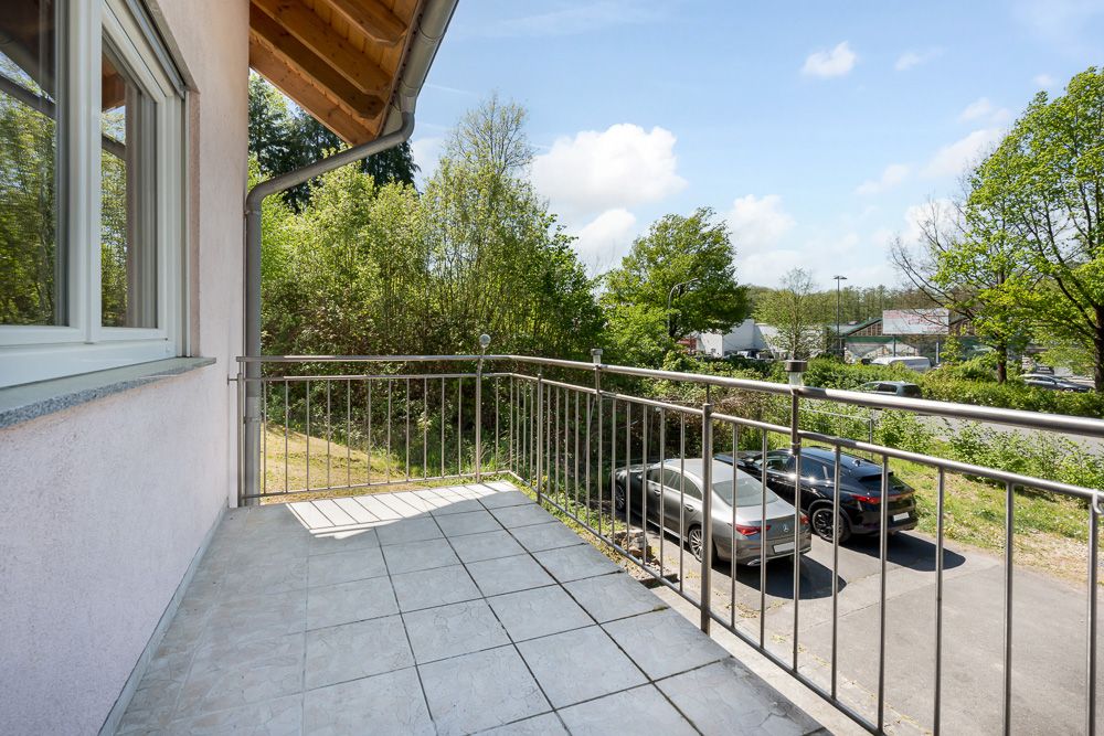 Balkon mit Metallgeländer und Blick auf parkende Autos und Bäume.