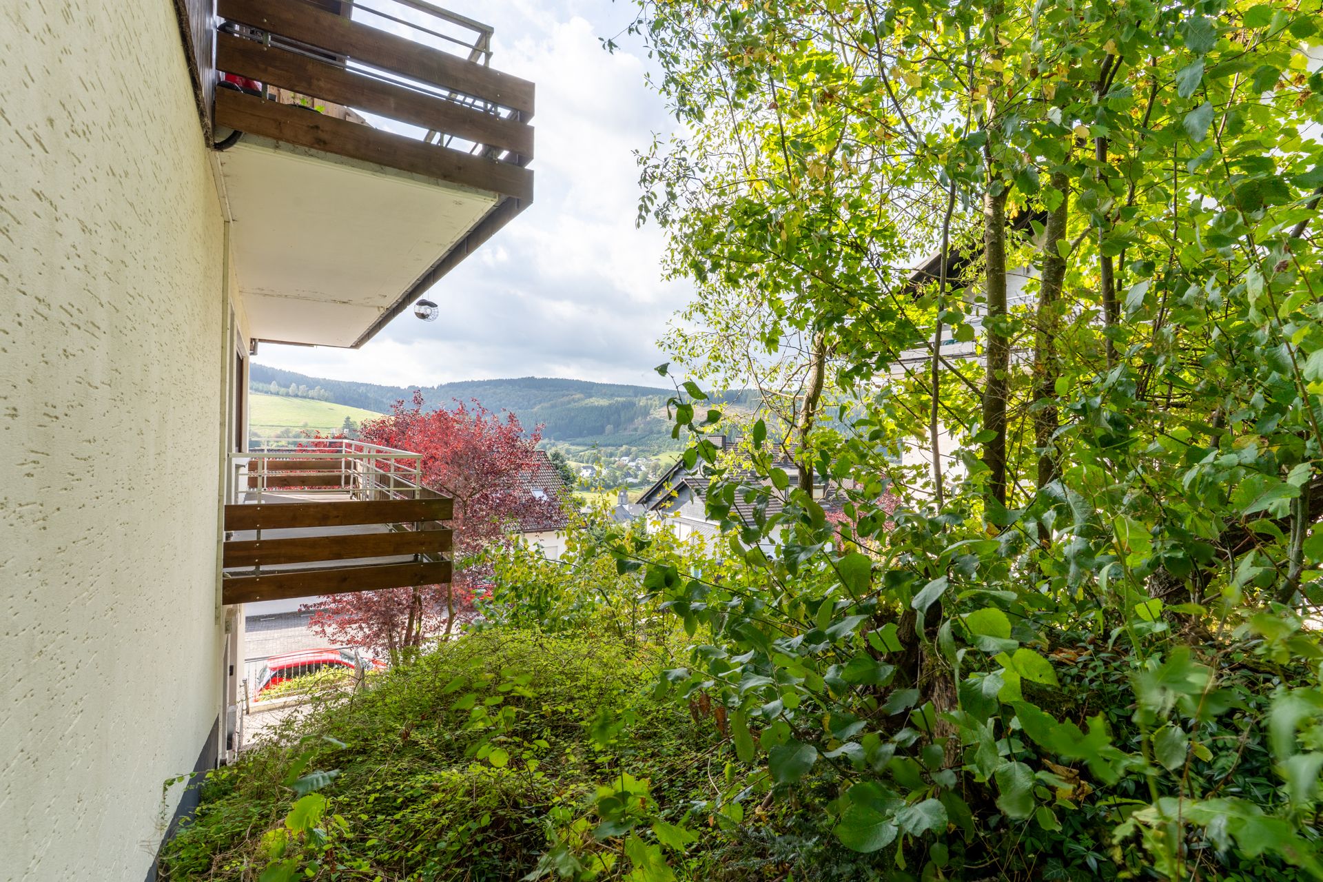 Balkon an einem Wohngebäude mit Ausblick auf grüne Bäume und Hügel im Hintergrund.