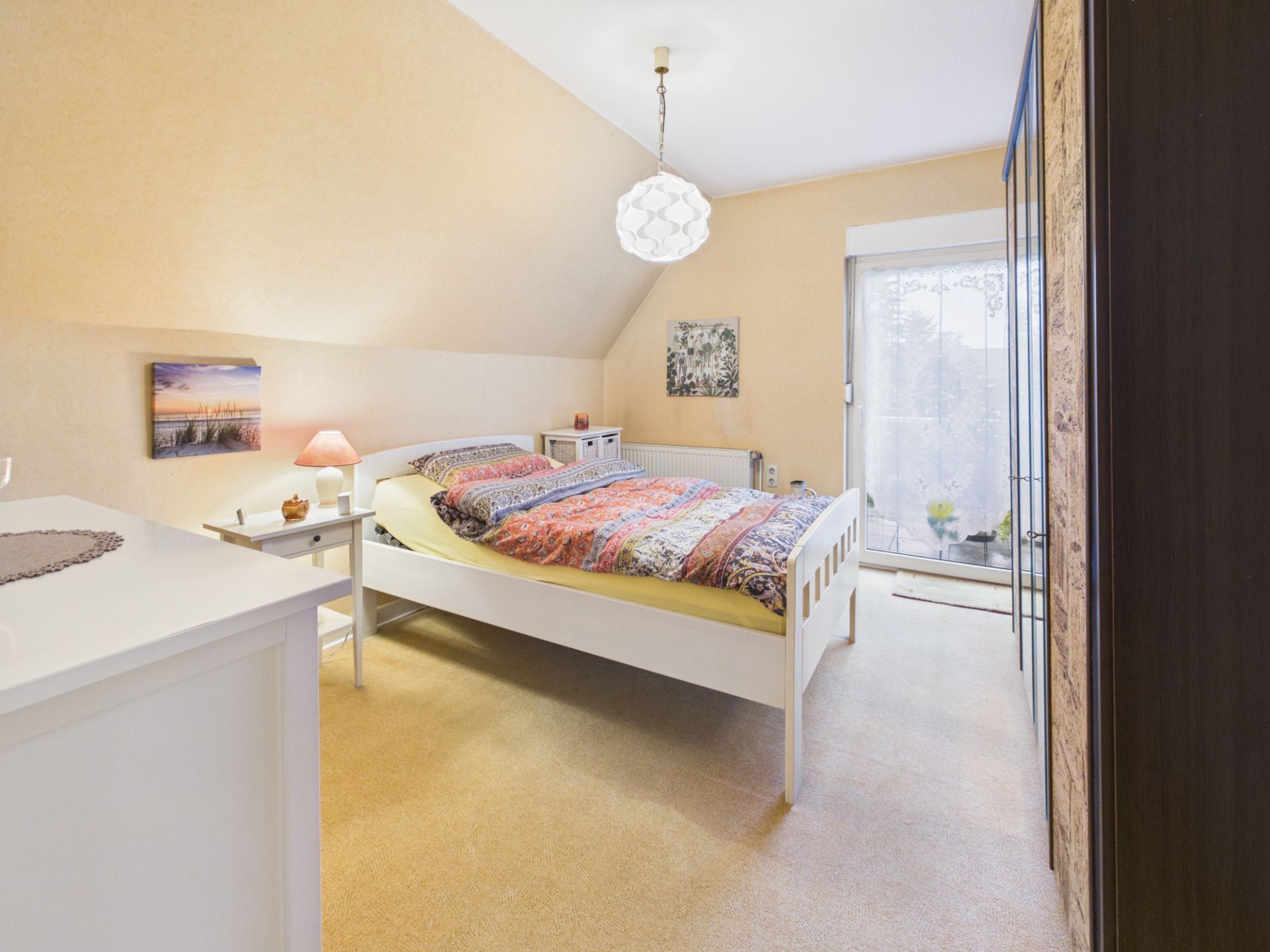 Helles Schlafzimmer mit Doppelbett, Nachttischen und Kleiderschrank, Zugang zum Balkon.