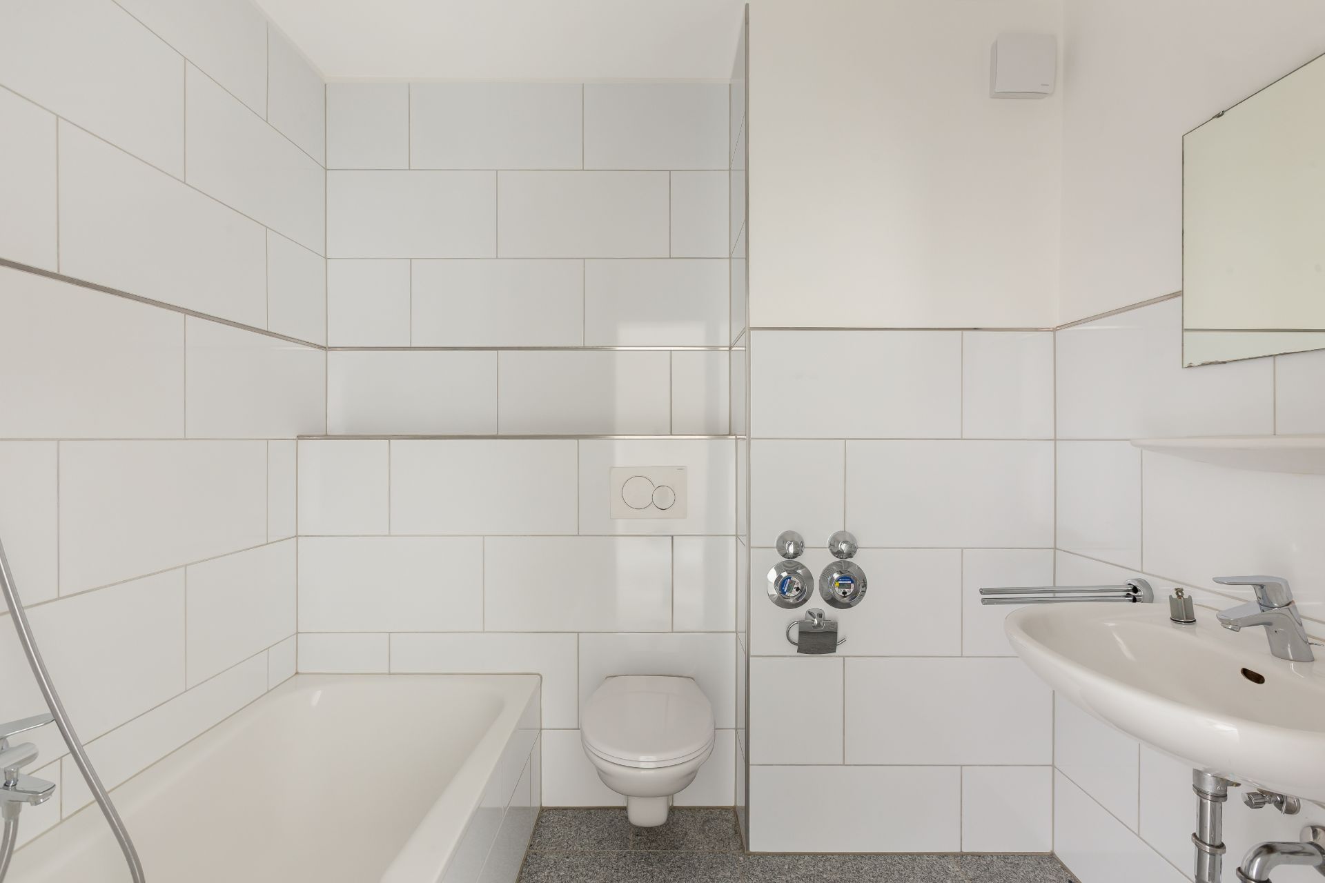 Helles Badezimmer mit Badewanne, Wand-WC, Waschbecken und Spiegel.