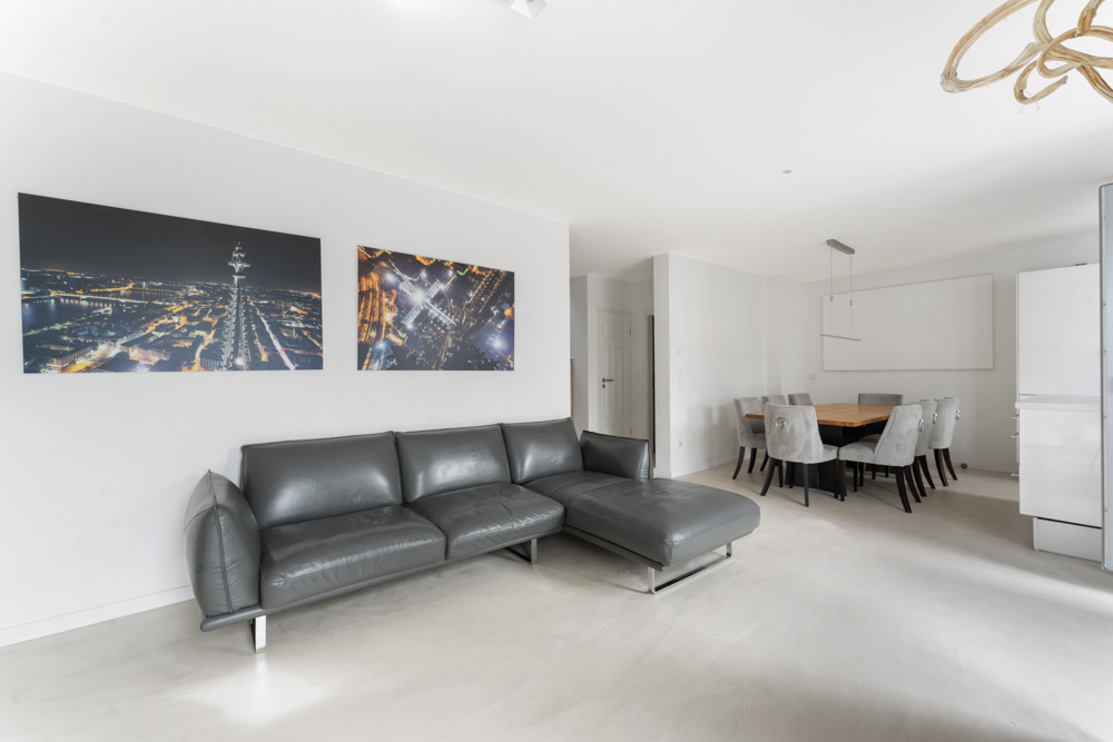 Modernes Wohnzimmer mit grauem Sofa und Esstisch mit acht Stühlen in hellem Raum.