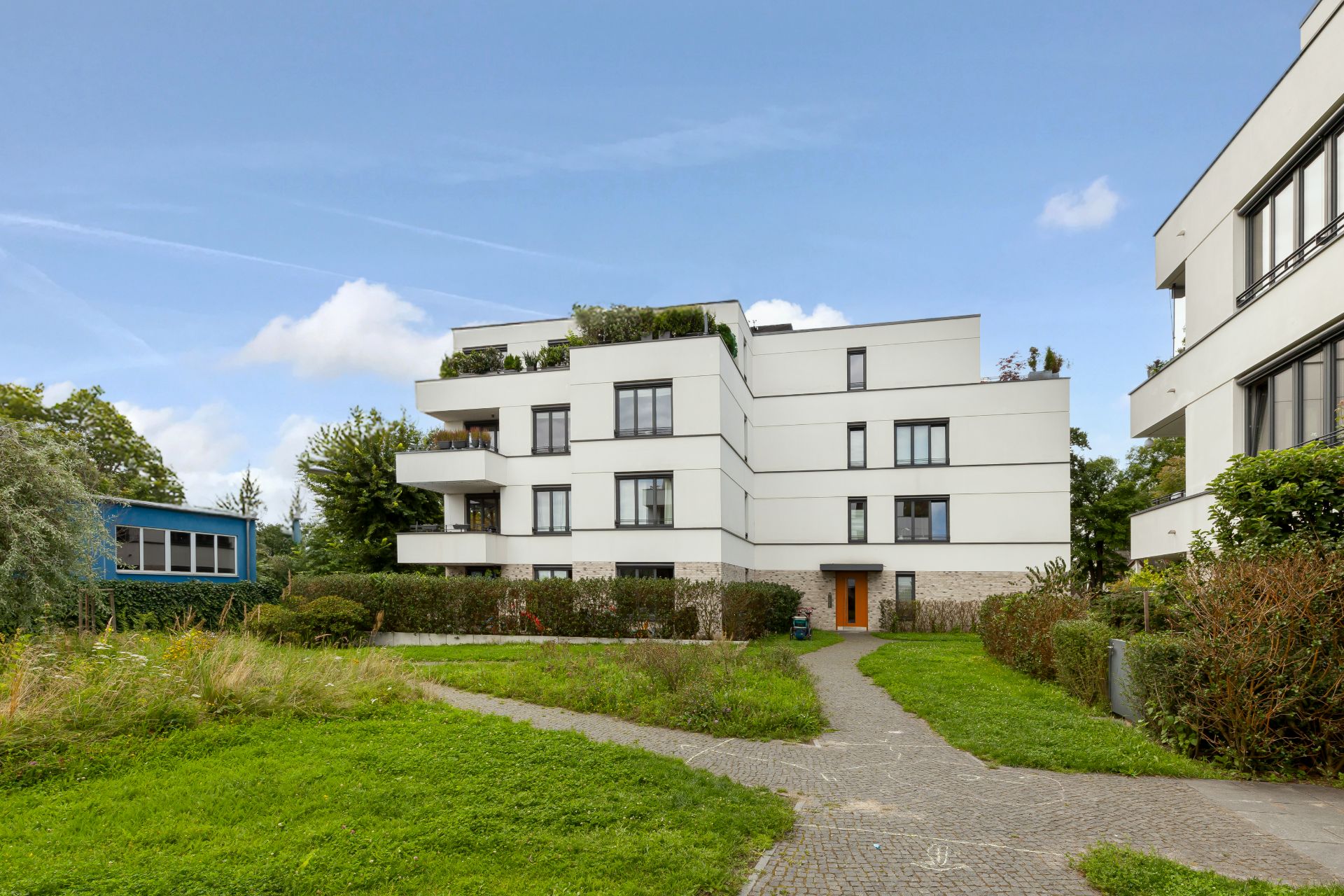 Modernes, weißes Wohngebäude mit mehreren Balkonen und gepflegtem Garten davor.
