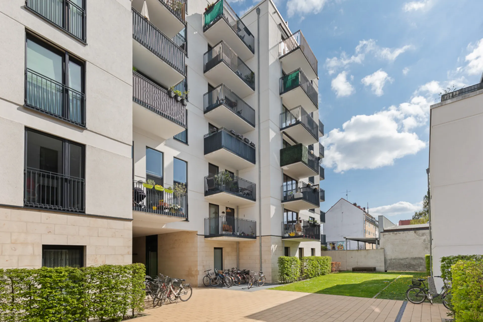 Moderner Wohnhauskomplex mit Balkonen, Fahrrädern und kleinem Innenhof bei sonnigem Wetter.