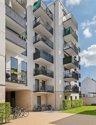 Moderner Wohnhauskomplex mit Balkonen, Fahrrädern und kleinem Innenhof bei sonnigem Wetter.
