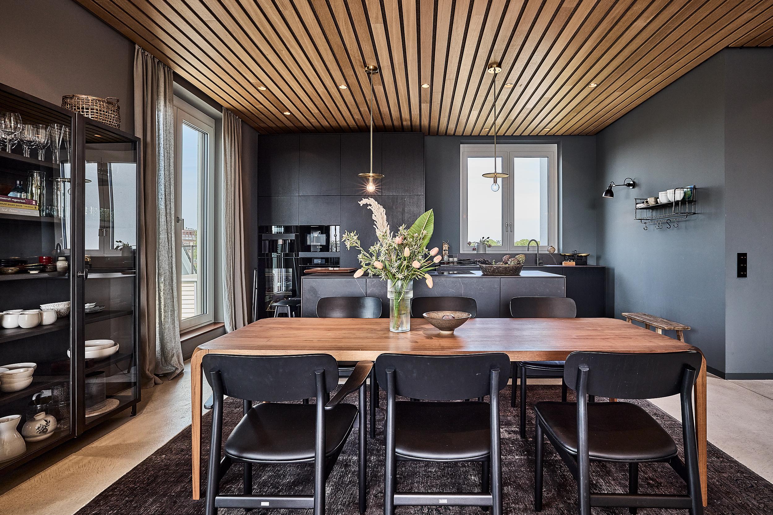 Moderne Küche mit Holztisch, schwarzen Stühlen und einem Blumenstrauß auf dem Tisch.