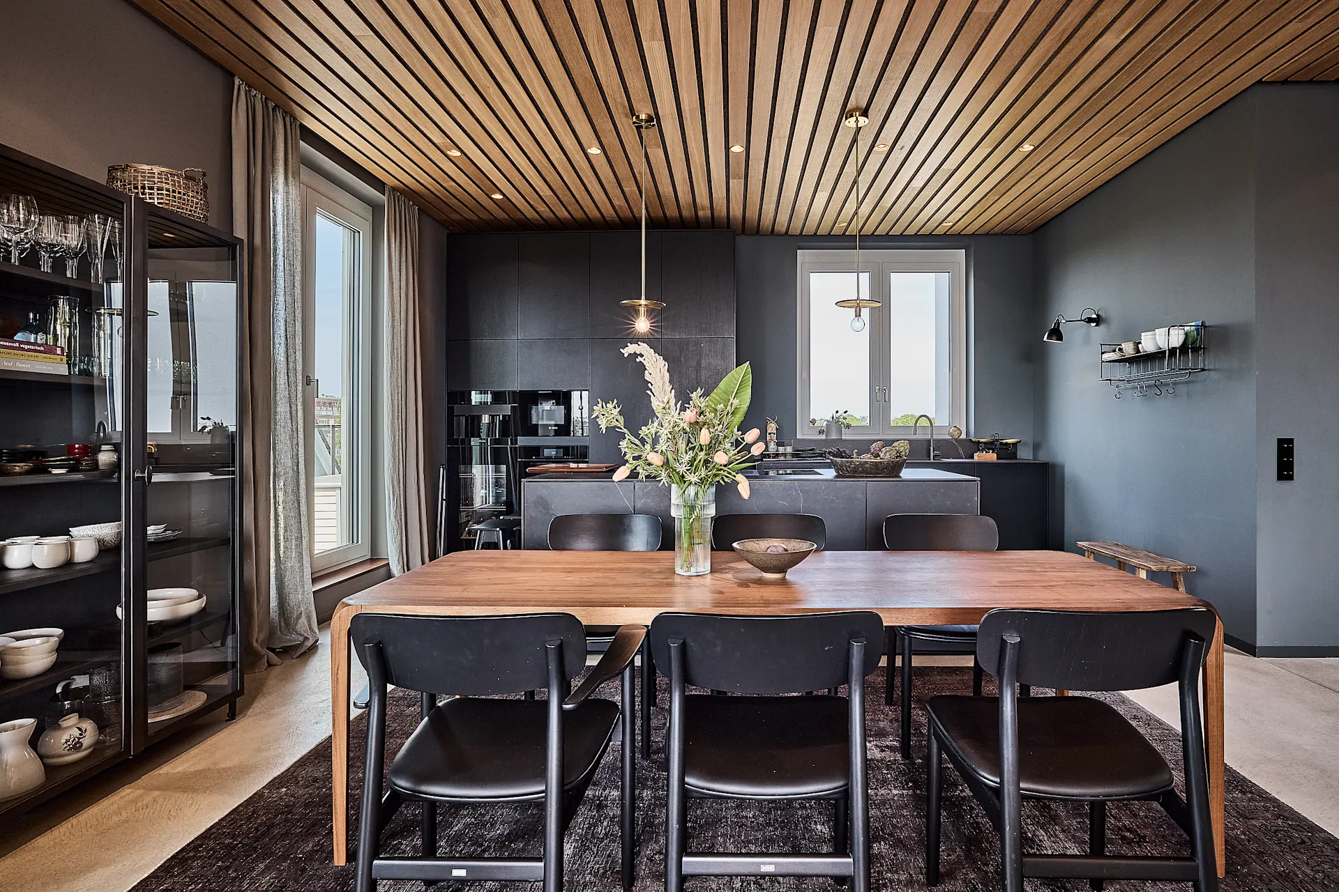 Moderne Küche mit Holztisch, schwarzen Stühlen und einem Blumenstrauß auf dem Tisch.