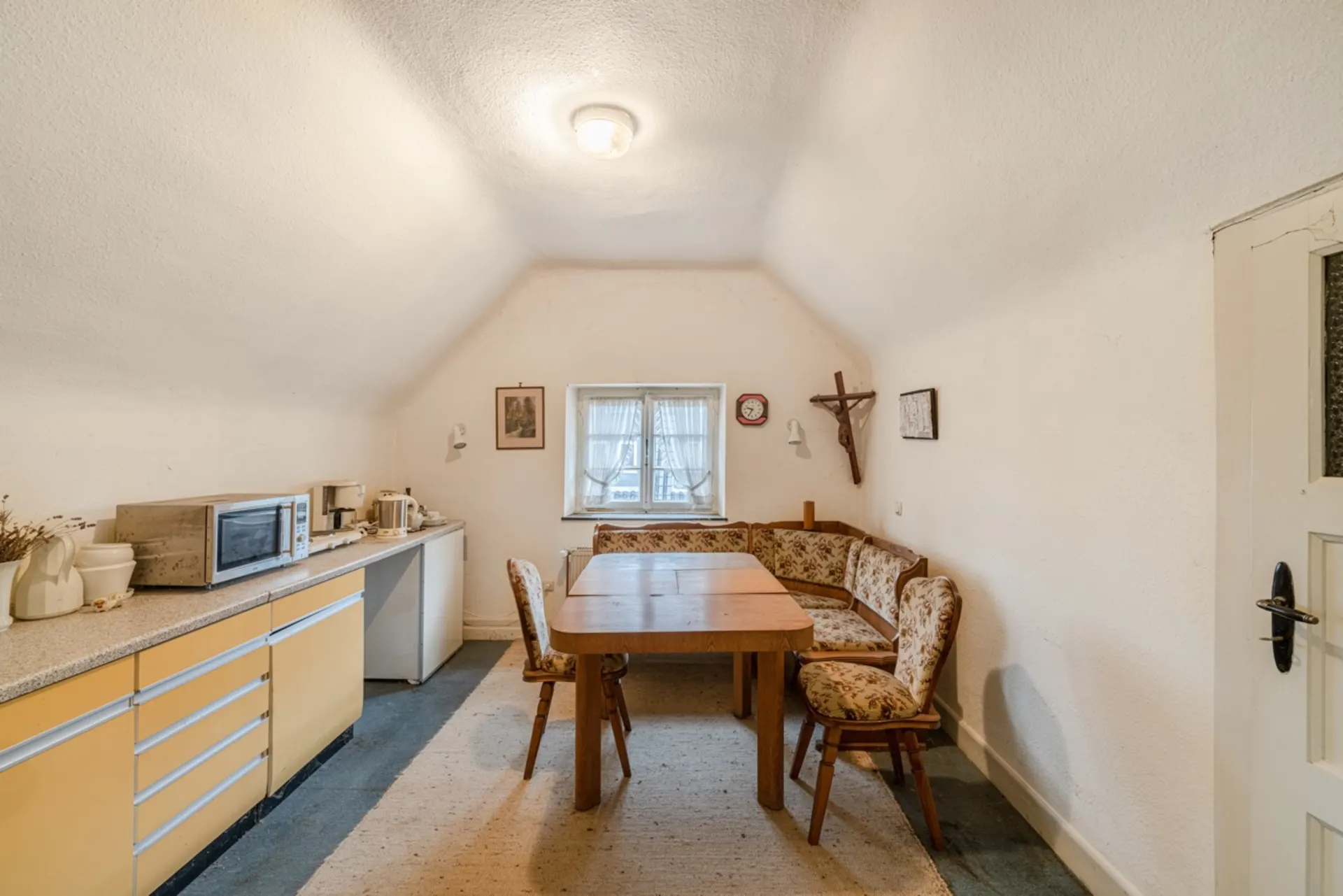 Küche mit gelben Schränken, Eckbank, Holztisch und Stühlen unter schräger Decke.