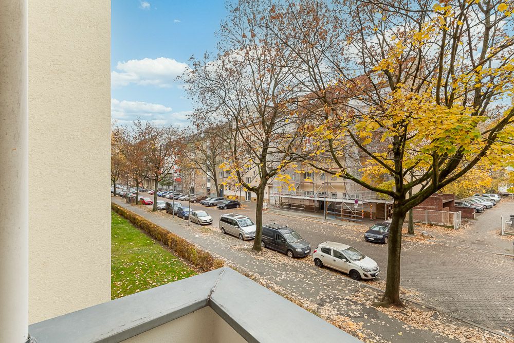 Aussicht vom Balkon auf eine Straße mit parkenden Autos und Bäumen mit Herbstlaub.