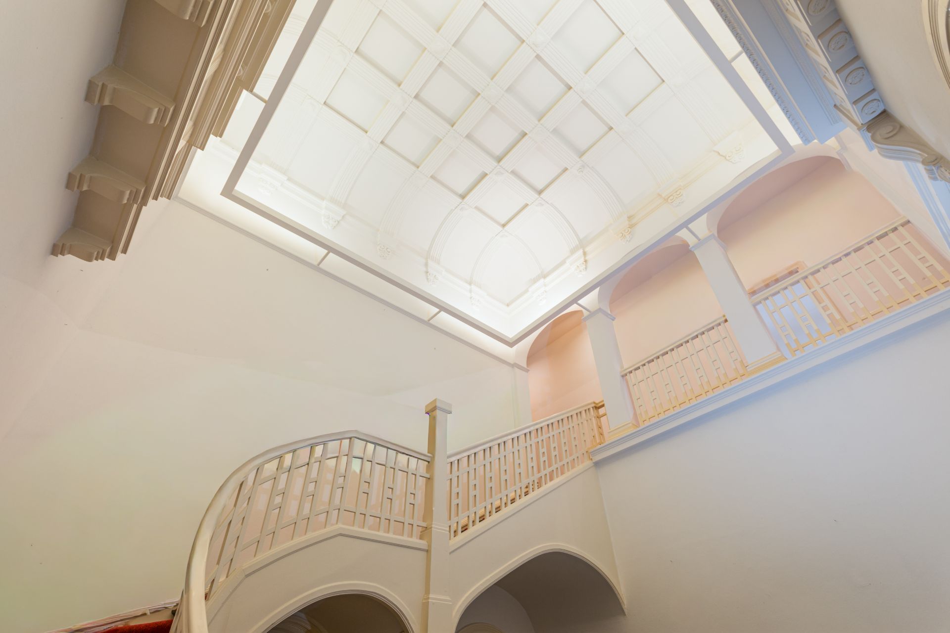 Helles Treppenhaus mit geschwungener Treppe, Oberlichtern und Geländern.