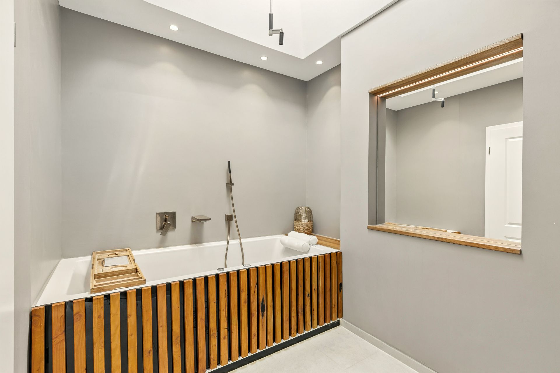 Modernes Badezimmer mit Badewanne mit Holzverkleidung und großem Wandspiegel.