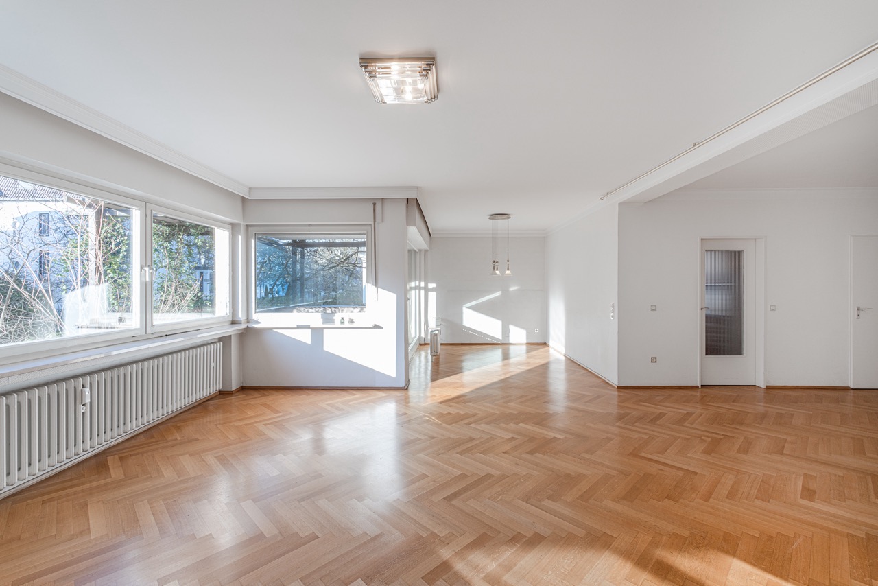 Helles Wohnzimmer mit Parkettboden, großen Fenstern und zwei weißen Türen.