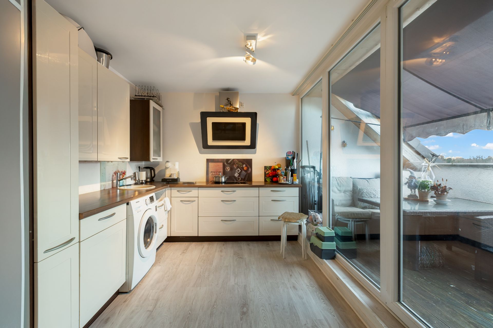 Moderne helle Küche mit Waschmaschine, großem Fenster und Zugang zum Balkon.