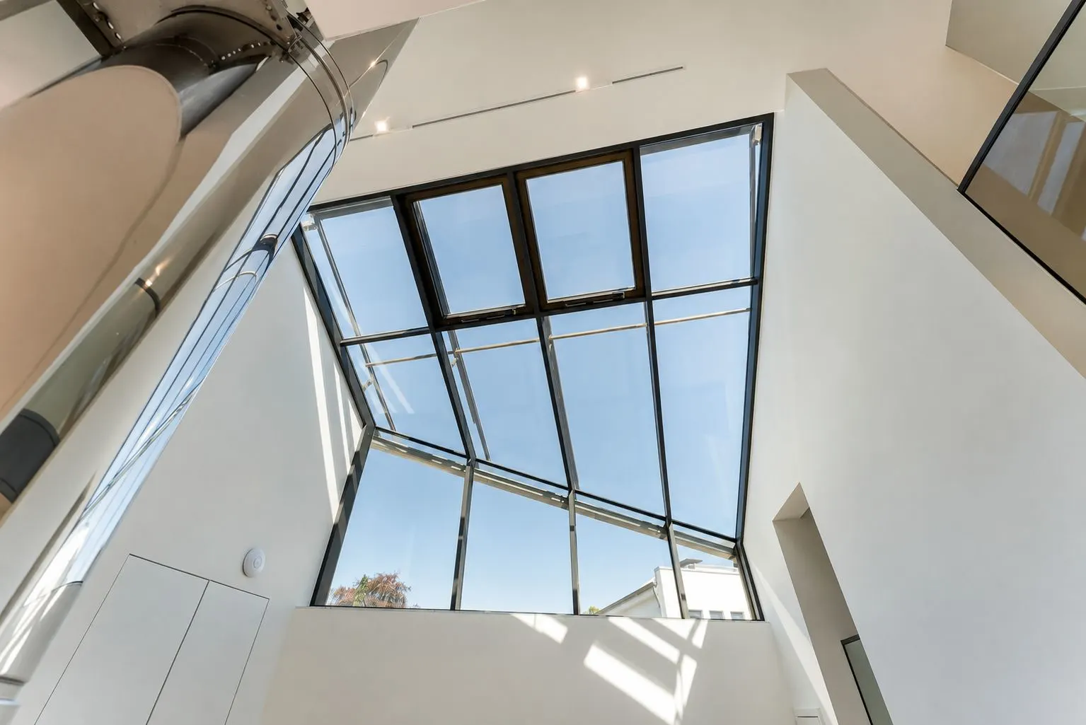 Großes Glasdach in einem modernen, hellen Wohnraum mit weißen Wänden.