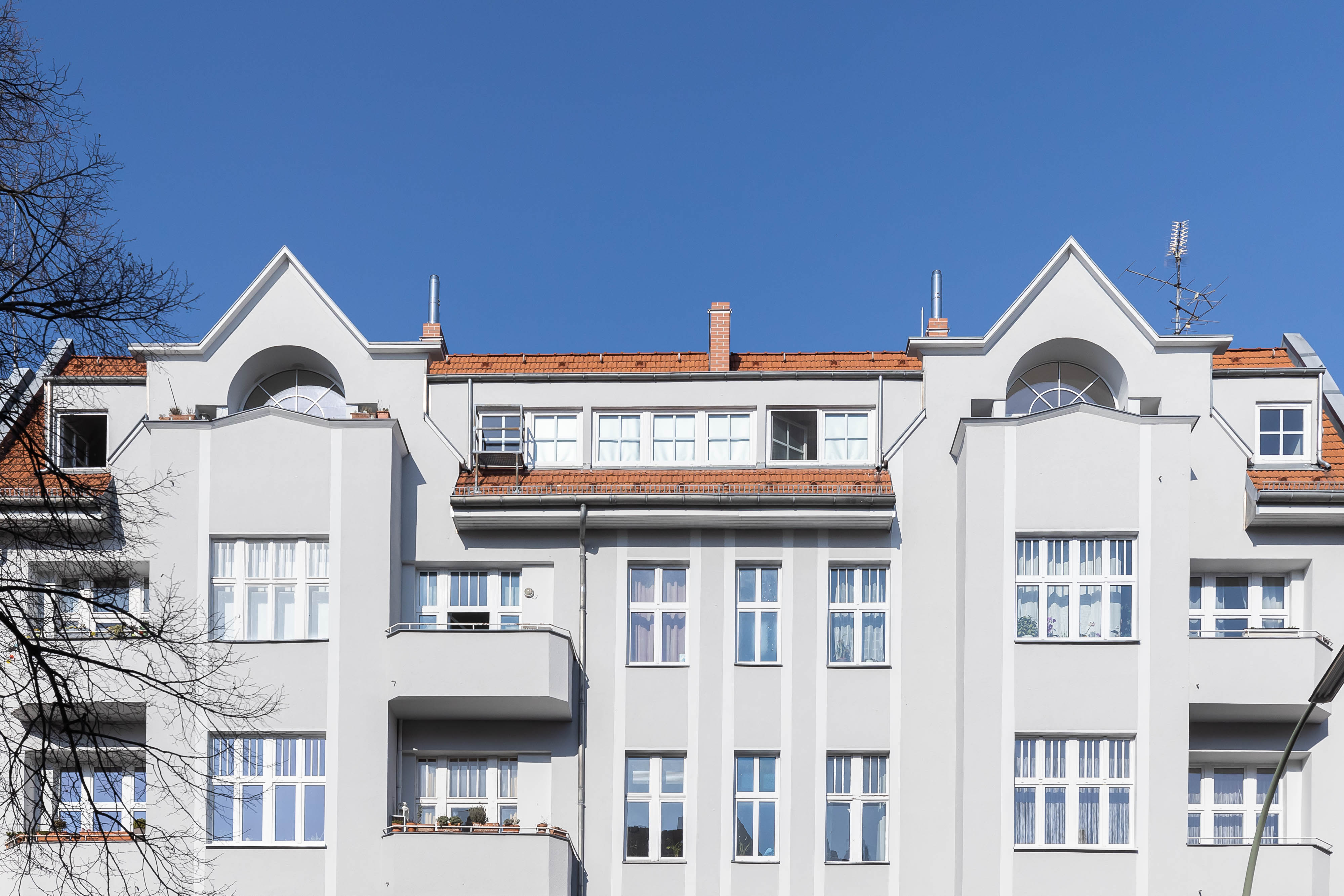 Fassade eines mehrstöckigen Wohngebäudes mit weißen Wänden und roten Dächern bei blauem Himmel.