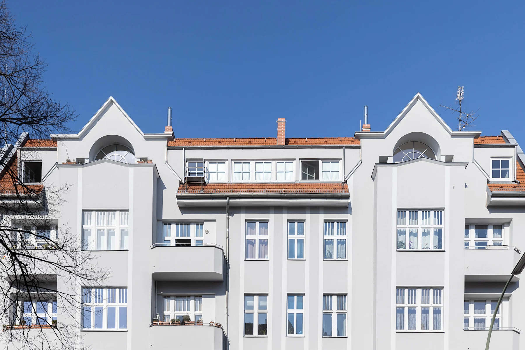 Fassade eines mehrstöckigen Wohngebäudes mit weißen Wänden und roten Dächern bei blauem Himmel.