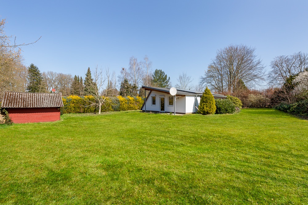 Haus mit Satellitenschüssel und rotem Schuppen auf großem, grünen Rasen bei sonnigem Wetter.