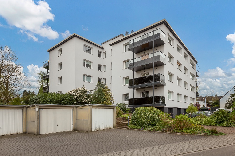 Mehrfamilienhaus mit weißen Fassaden und Balkonen, davor Garagen und Grünanlagen.