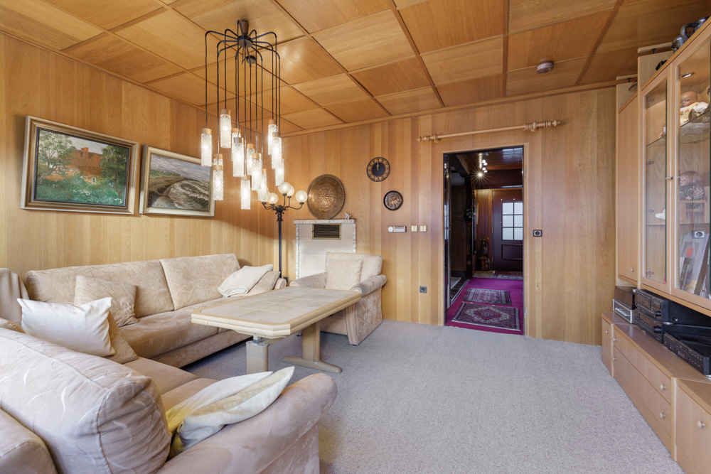 Wohnzimmer mit beigen Sofas, Holzwänden, Bildern, Glastisch und moderner Hängelampe.