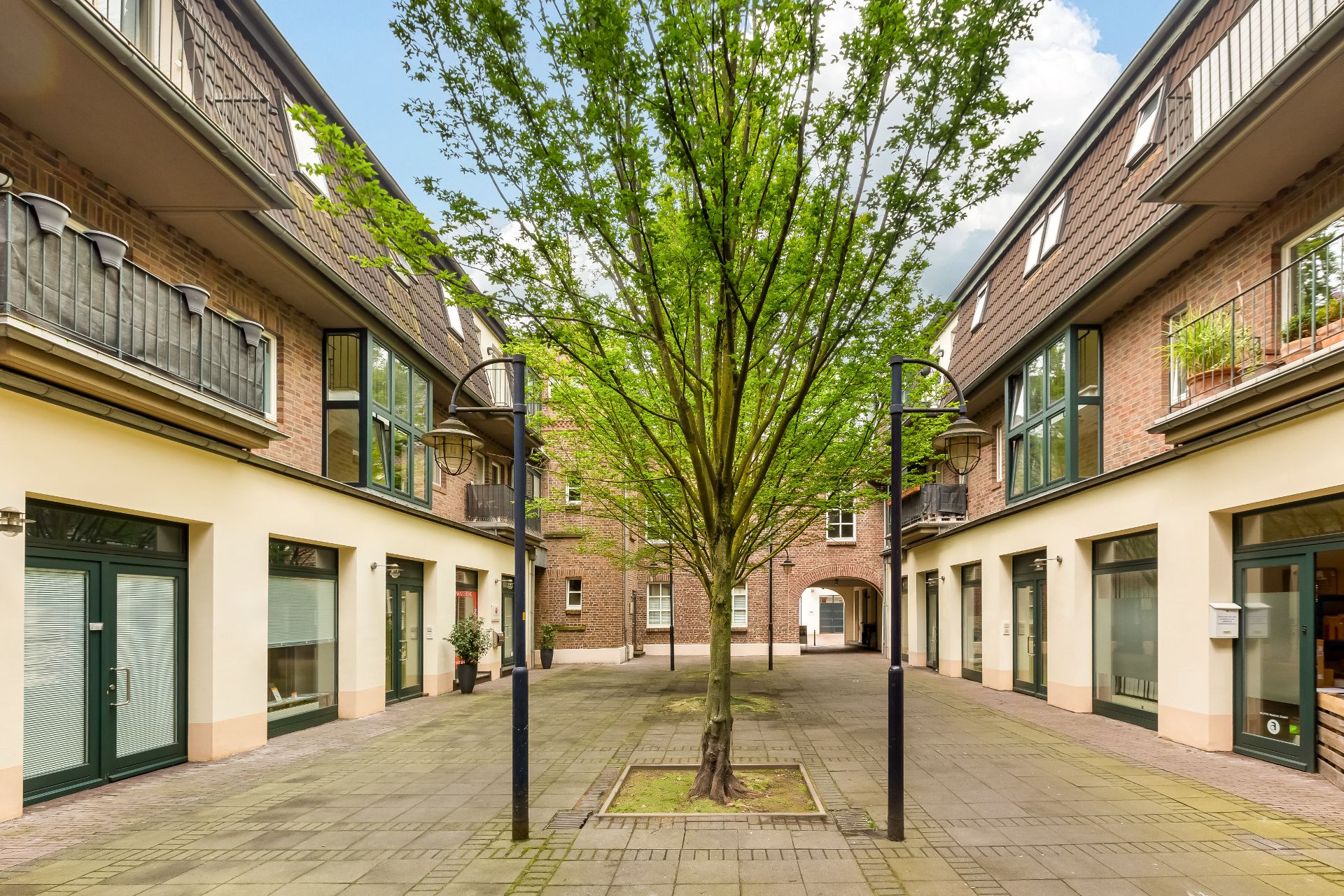 Innenhof mit gepflastertem Boden, Baum in der Mitte und umliegenden Wohngebäuden.