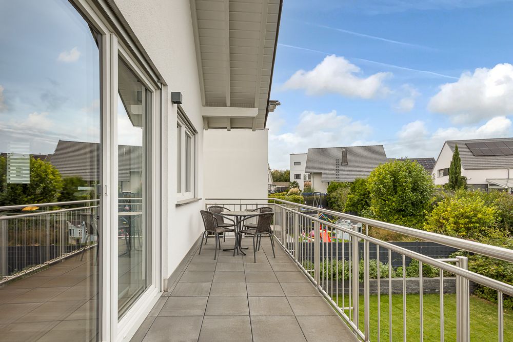 Großer Balkon mit Sitzgruppe, Blick auf Garten und Nachbarhäuser.