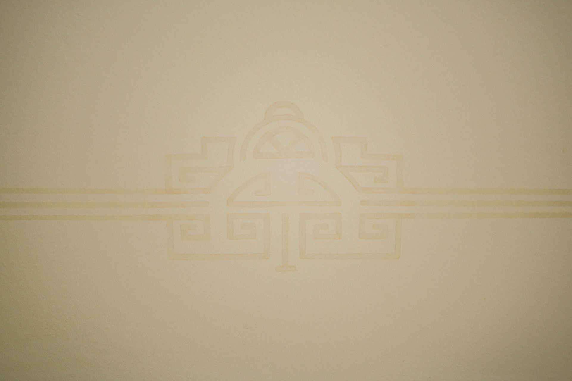 Beige Wand mit hellem, geometrischem Muster in der Mitte.