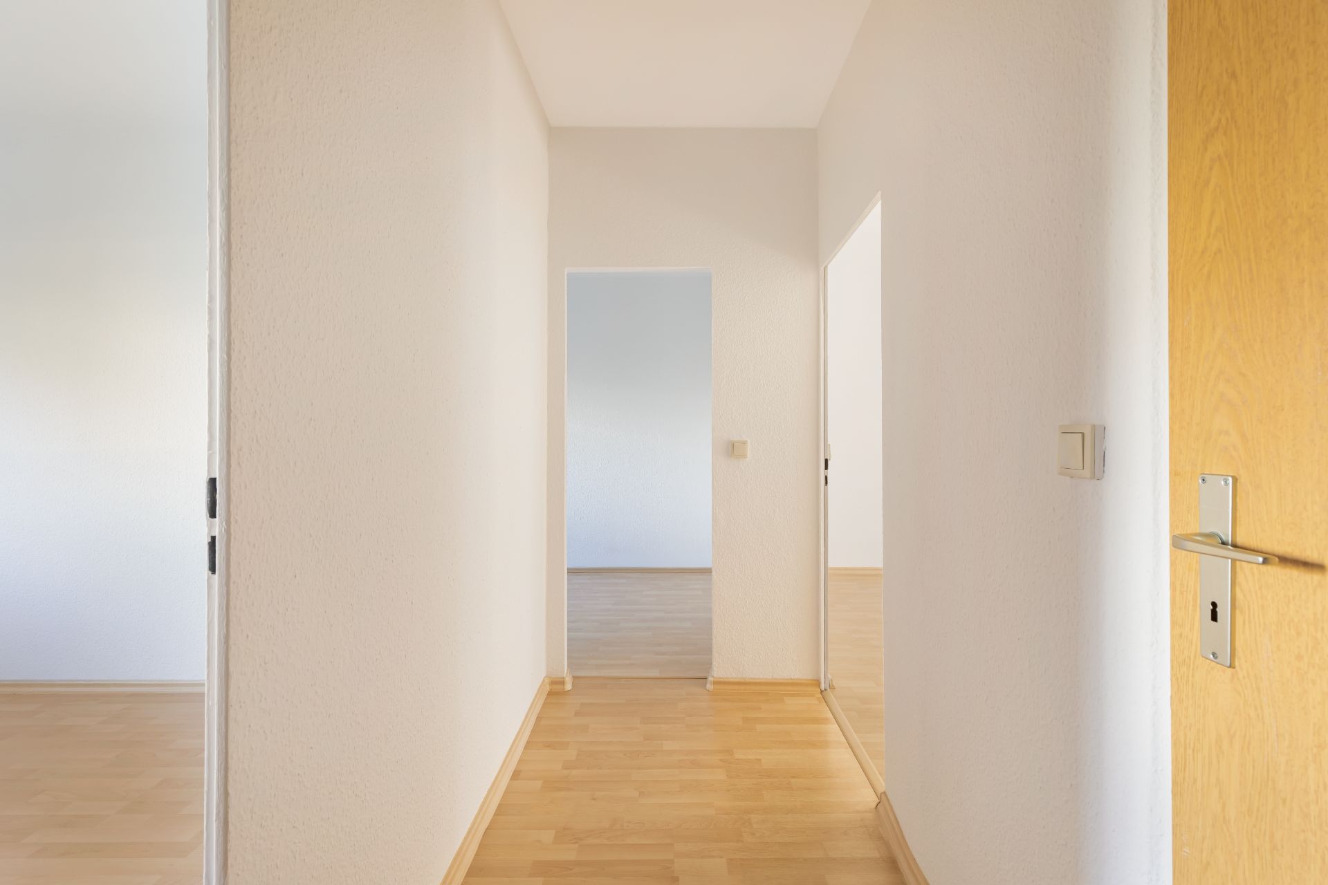 Heller Flur mit Holzboden und weißen Wänden, Türen führen in weitere Zimmer.