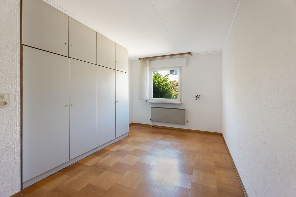 Helles Zimmer mit Einbauschrank, Fenster, Parkettboden und weiß gestrichenen Wänden.