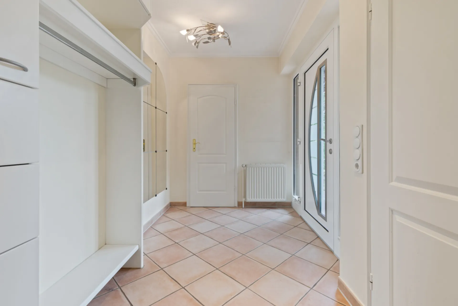 Heller Eingangsbereich mit Fliesenboden, Garderobe, Spiegelwand und Glastür.