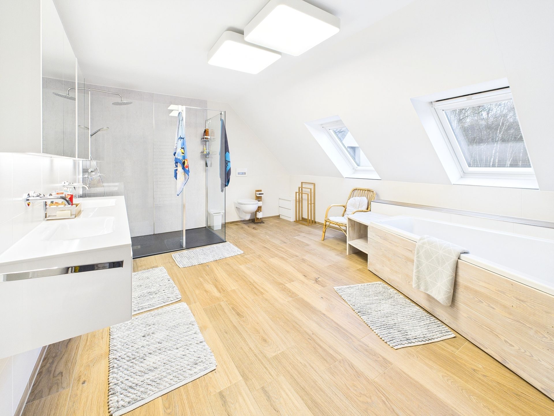 Helles Badezimmer mit Holzfußboden, Dusche, Badewanne und zwei Fenstern im Dach.
