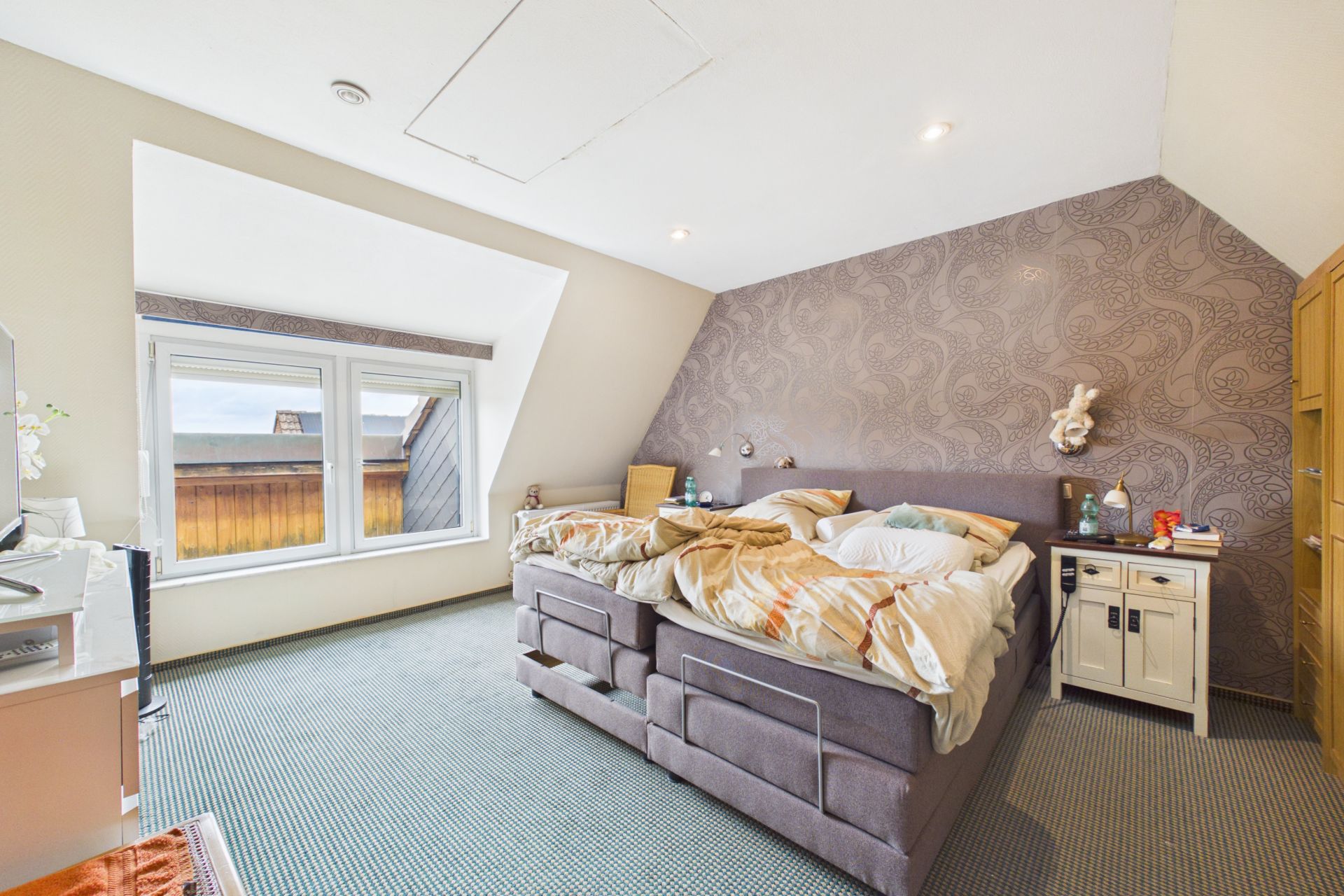 Helles Schlafzimmer mit großem Bett, gemusterter Wand und Fenster mit Holzrahmen.