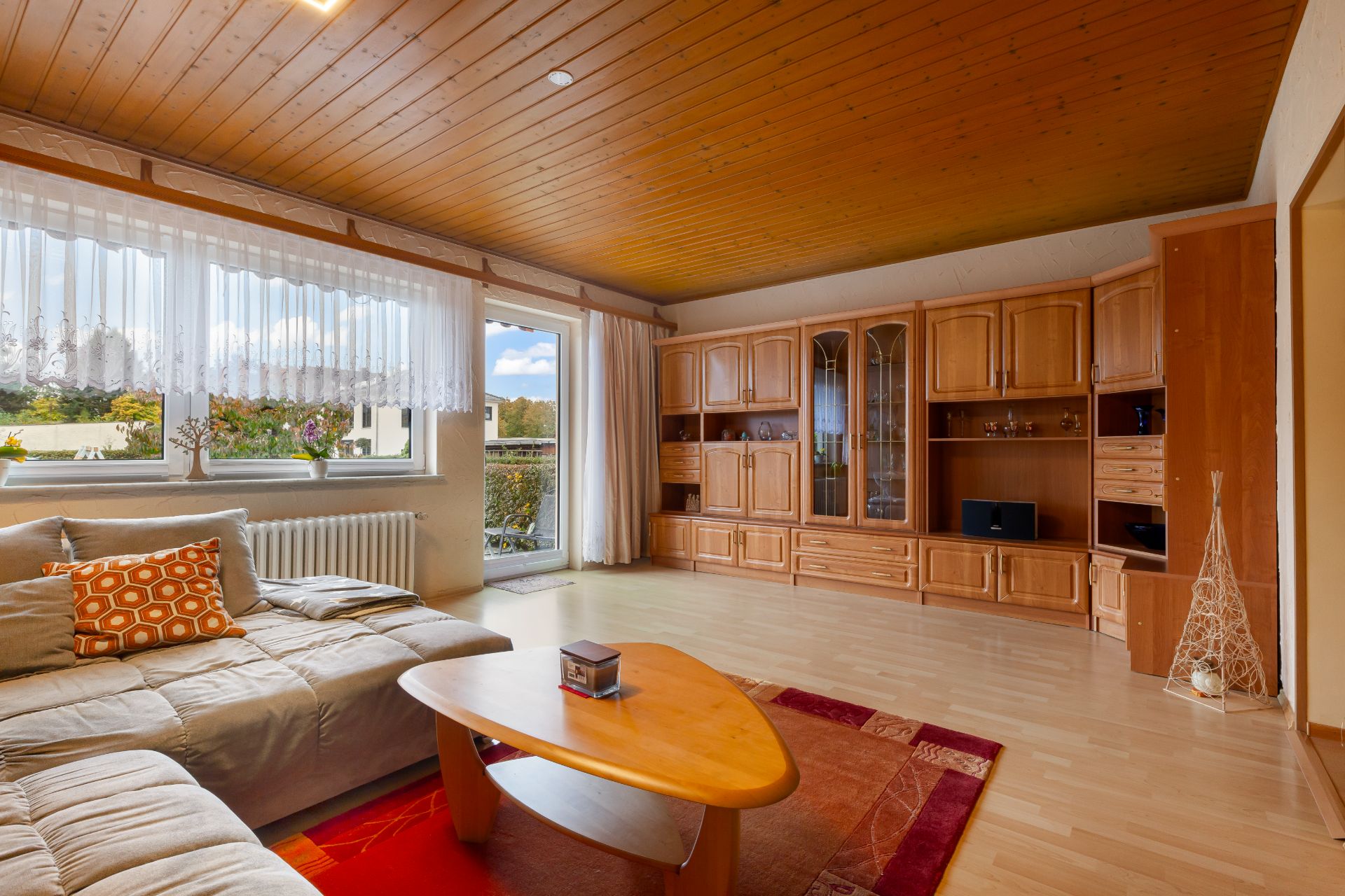 Helles Wohnzimmer mit großer Couch, Holztisch und Wohnwand, Blick auf Fenster und Balkon.