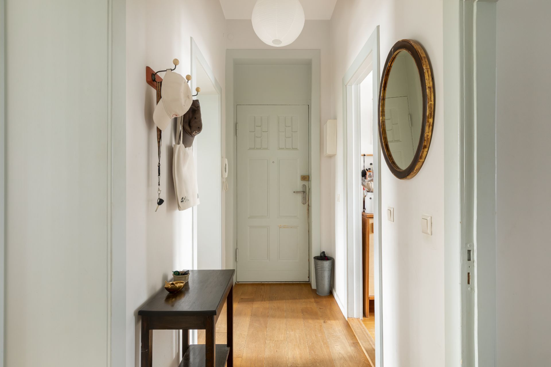 Heller Flur mit Holzboden, Garderobe, kleinem Tisch und rundem Spiegel an der Wand.