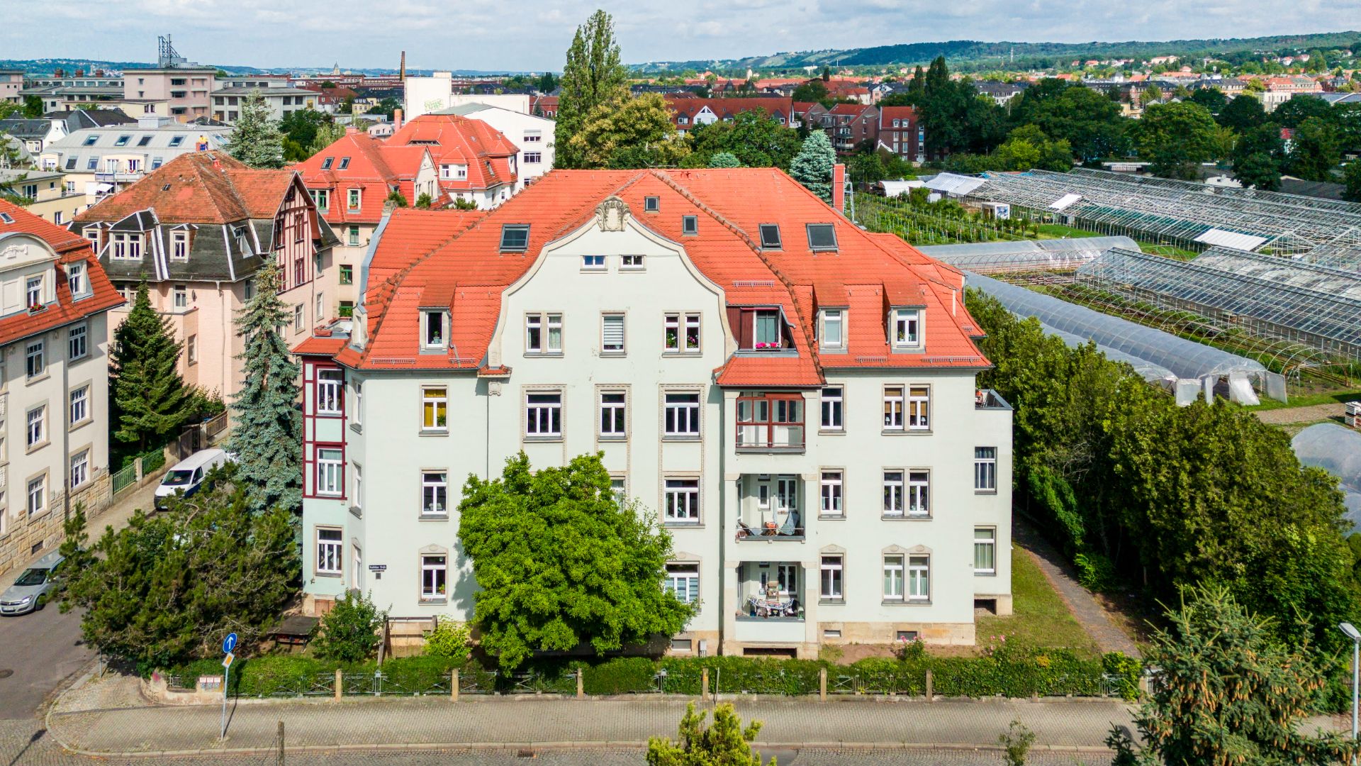 Mehrstöckiges Wohnhaus mit rotem Dach und Balkonen, umgeben von Bäumen.