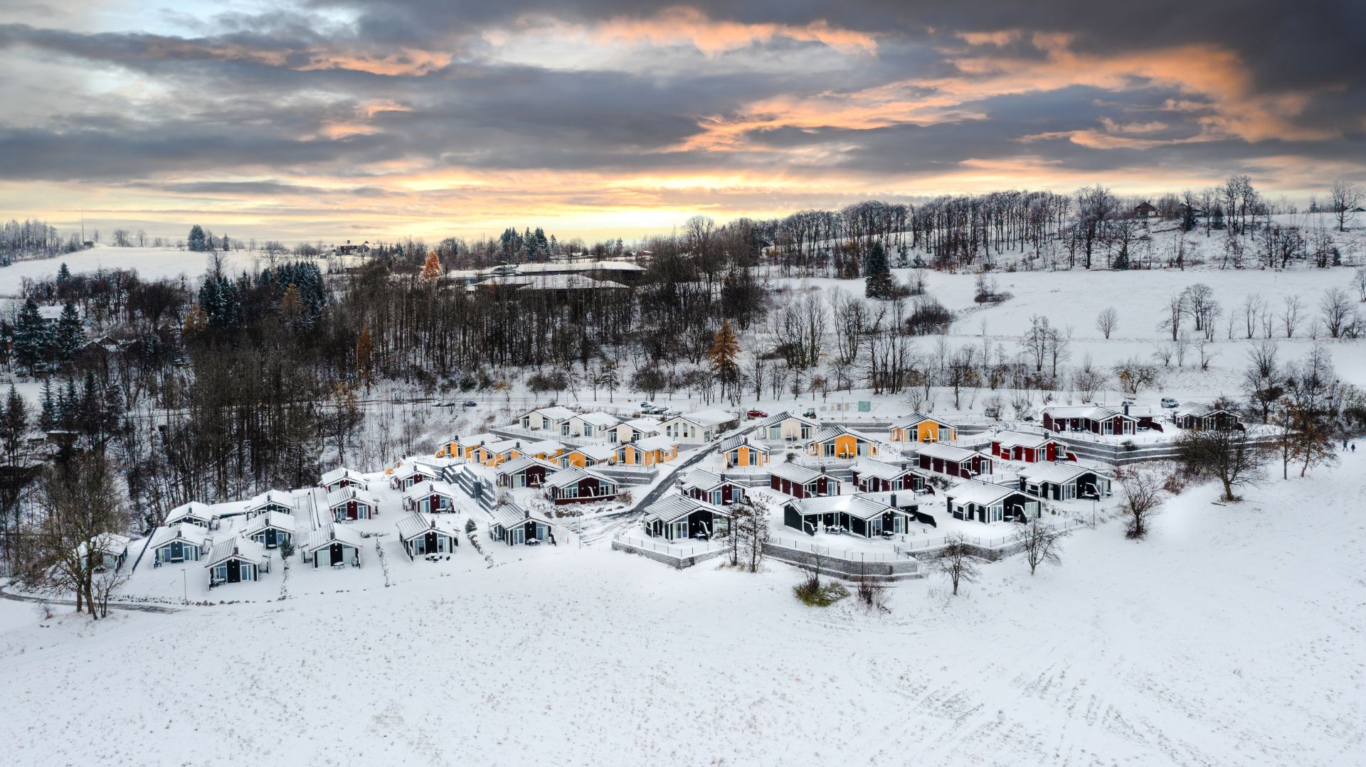 Luftaufnahme von kleinen Häusern in einer verschneiten Winterlandschaft bei Sonnenuntergang.