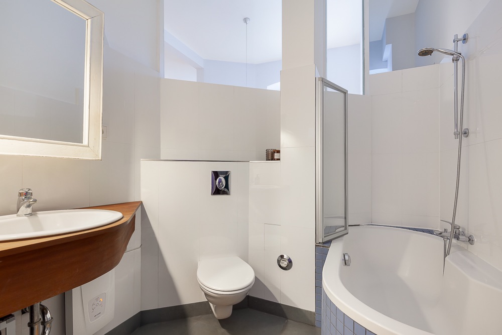Modernes Badezimmer mit Wandtoilette, Waschbecken und Eckbadewanne mit Duscharmatur.