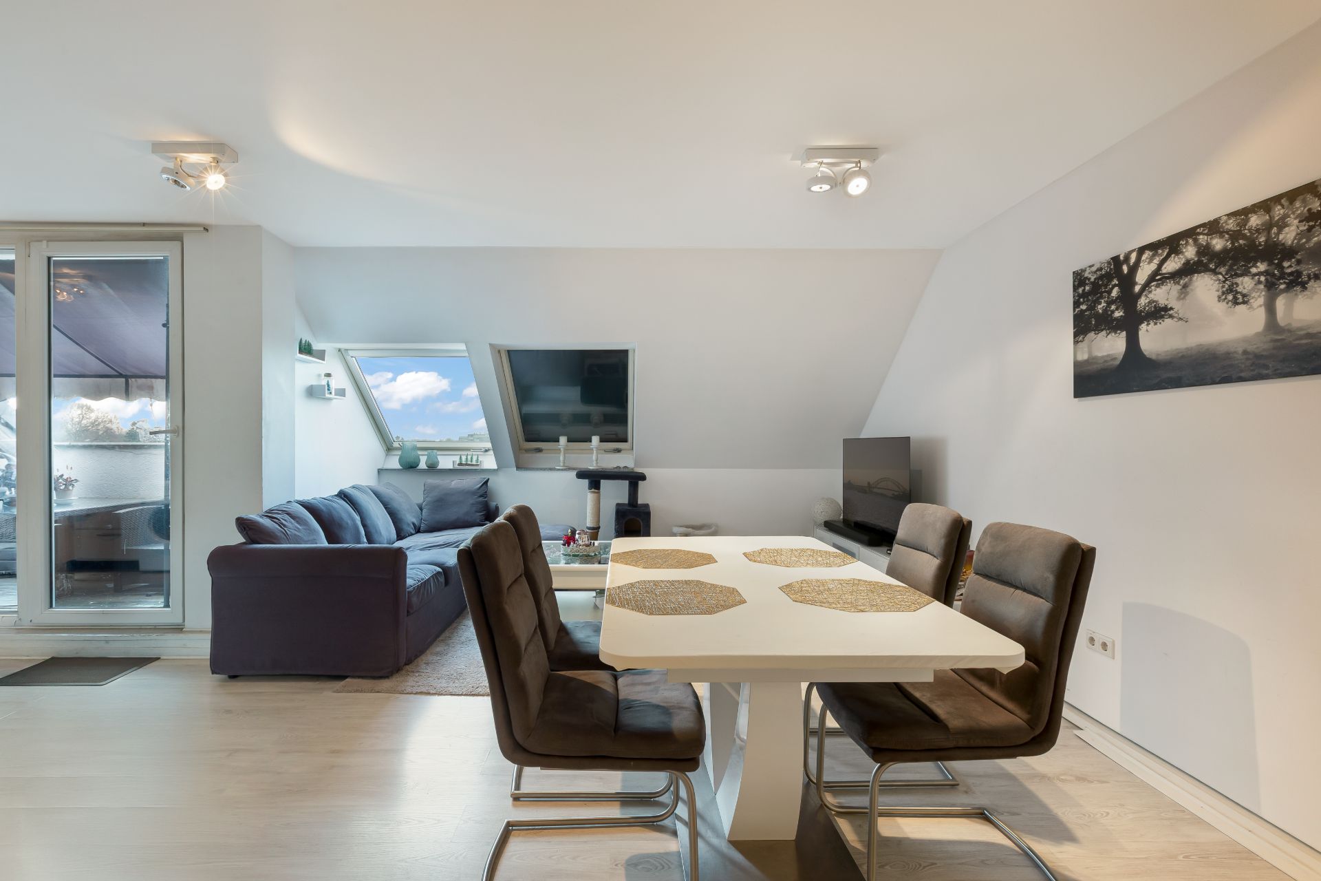Wohnzimmer mit Esstisch, vier Stühlen und Sofa, Zugang zum Balkon, großes Fenster.