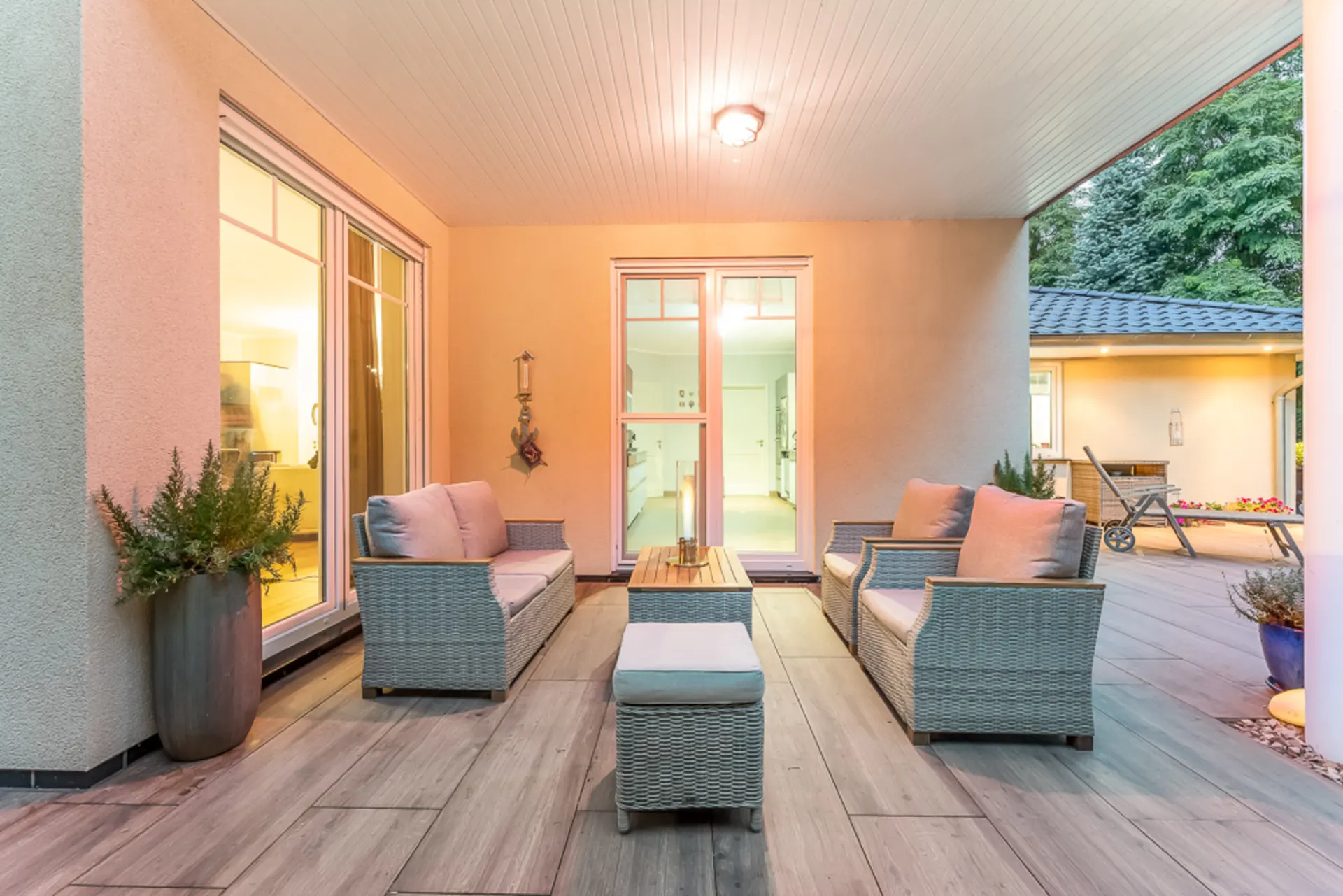 Überdachte Terrasse mit Sitzgruppe, Holztisch und Pflanzkübeln bei einem Wohnhaus.