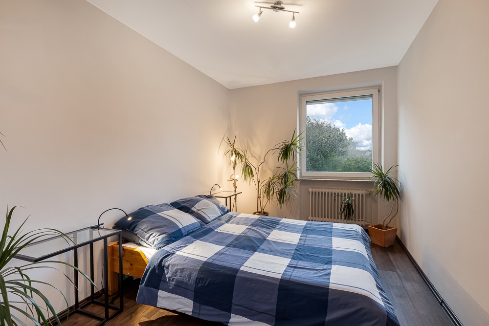 Schlafzimmer mit Doppelbett, Nachttischen, Pflanzen und Fenster mit Blick ins Grüne.