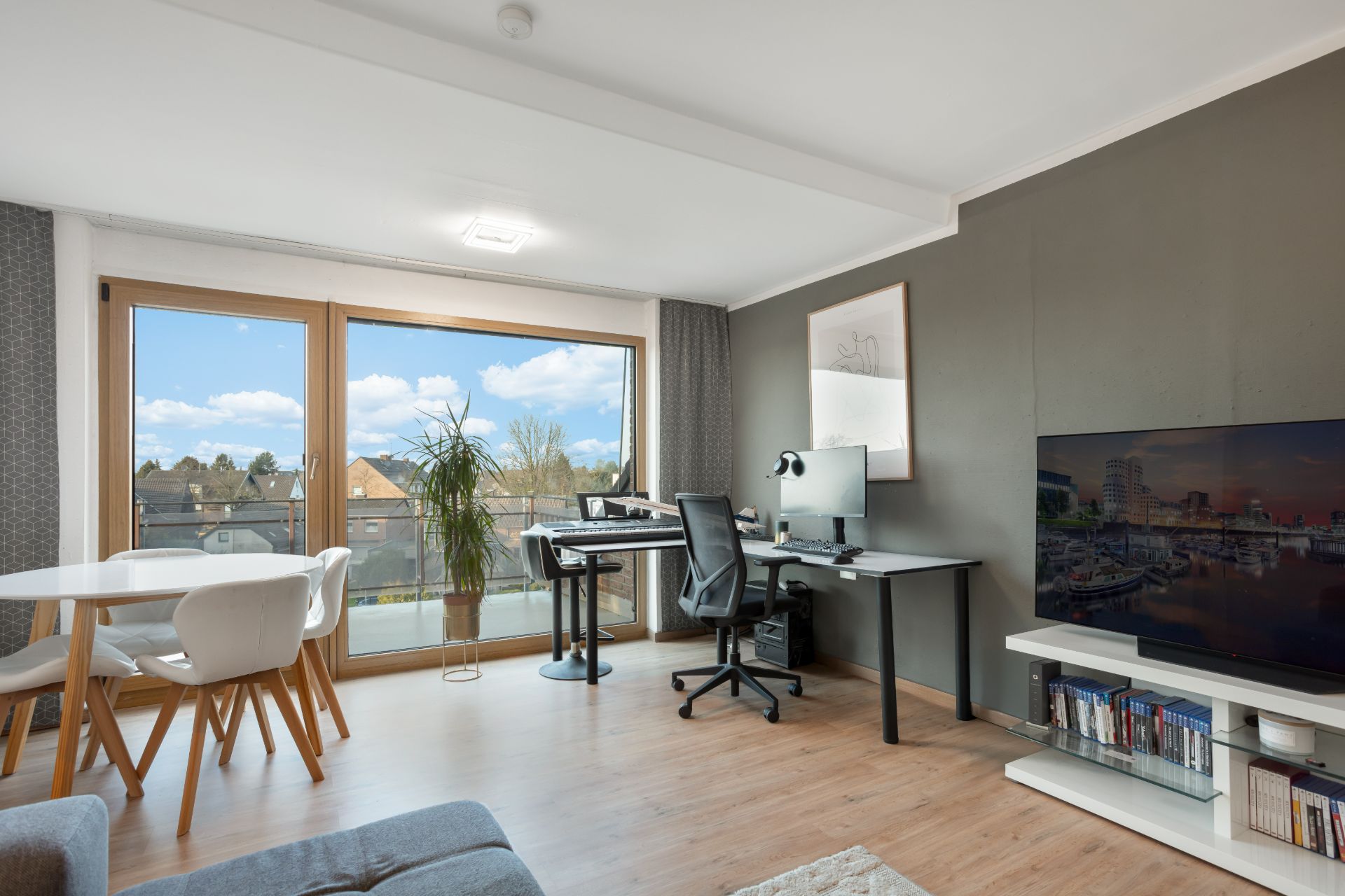 Helles Wohnzimmer mit Esstisch, Schreibtisch, Fernseher und großem Fenster.