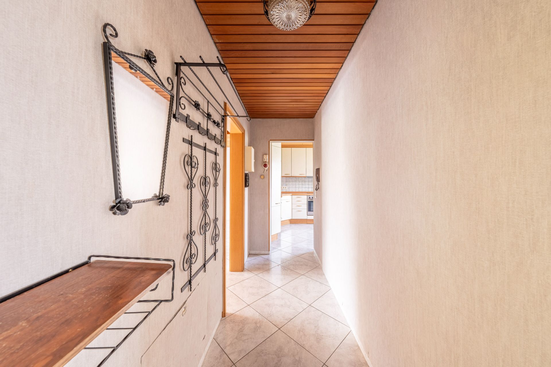 Heller Flur mit Fliesenboden, Holzbalkendecke, Spiegel und Garderobe, führt zur Küche.