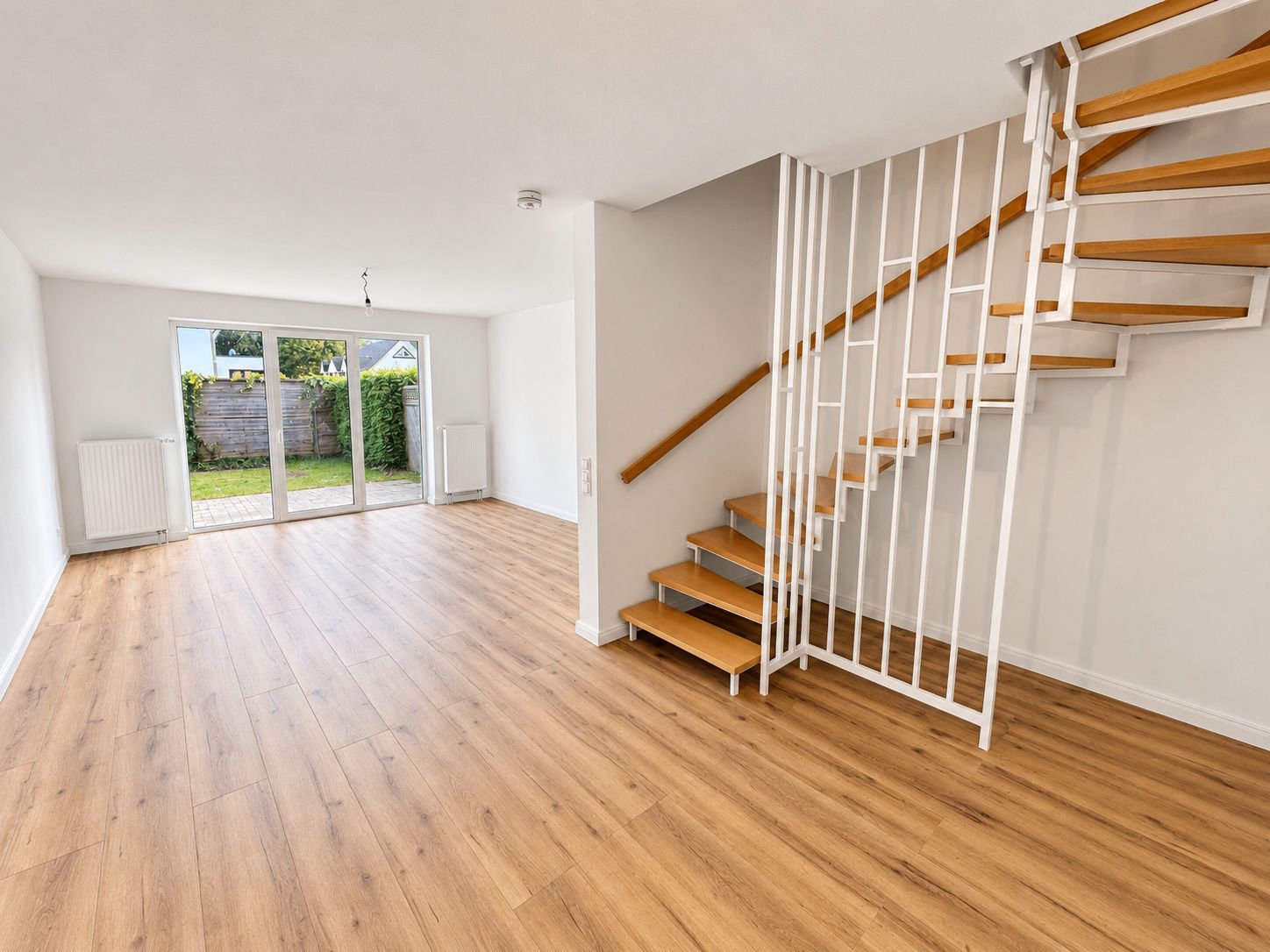 Helles Wohnzimmer mit Holzfußboden, moderner Treppe und großer Glastür zum Garten.