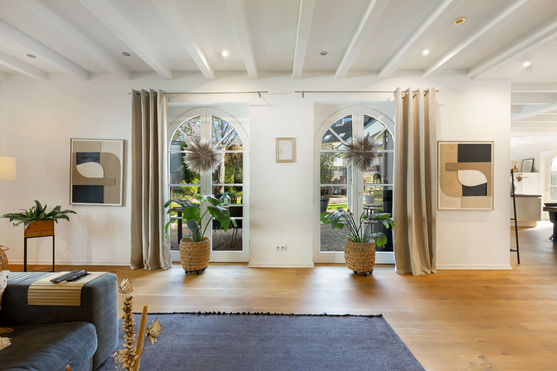 Helles Wohnzimmer mit Holzboden, großen Fenstern, Pflanzen und moderner Dekoration.