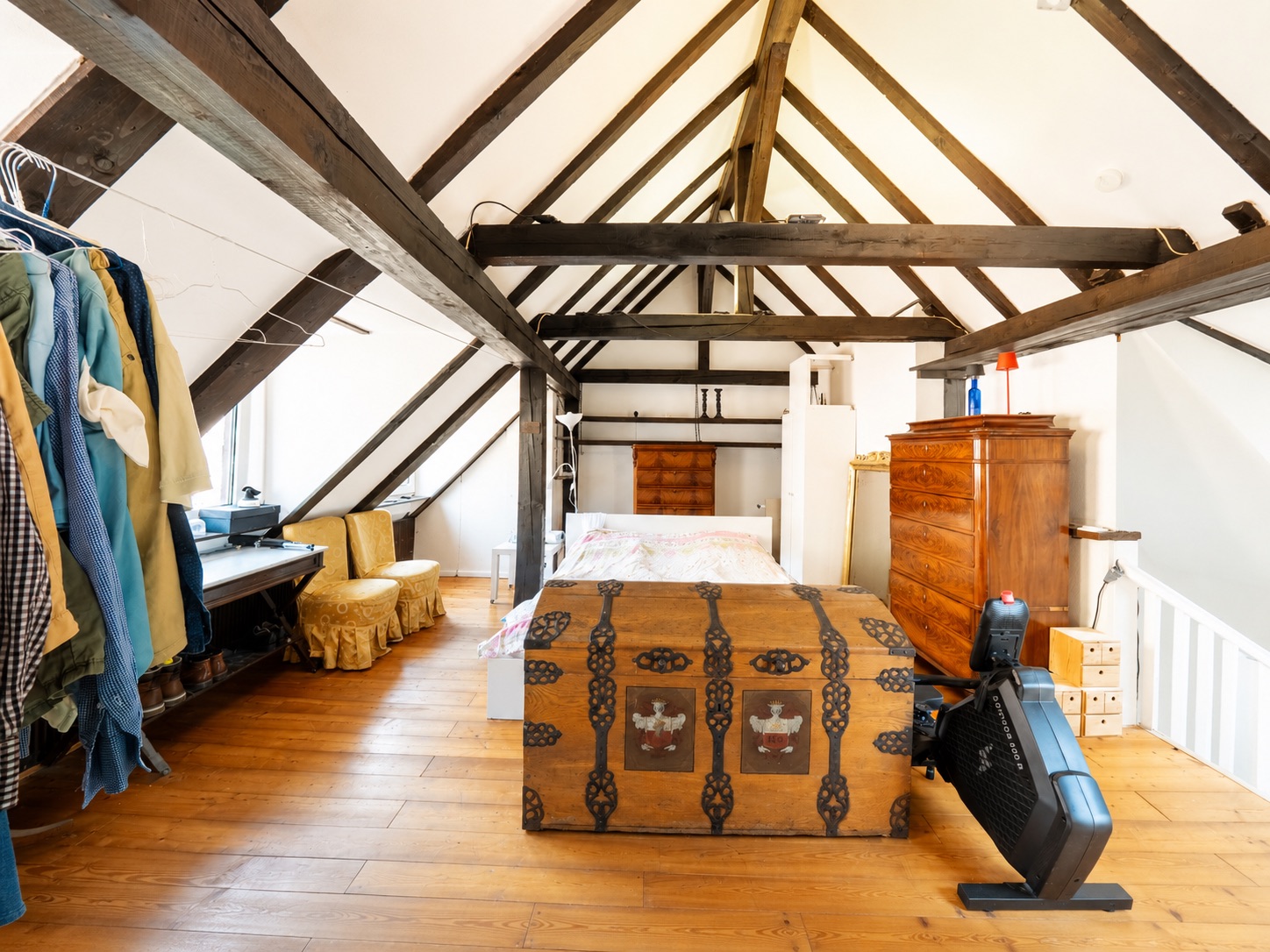 Dachgeschosszimmer mit Holzbalken, Bett, Kleiderschrank und Truhe auf Holzboden.